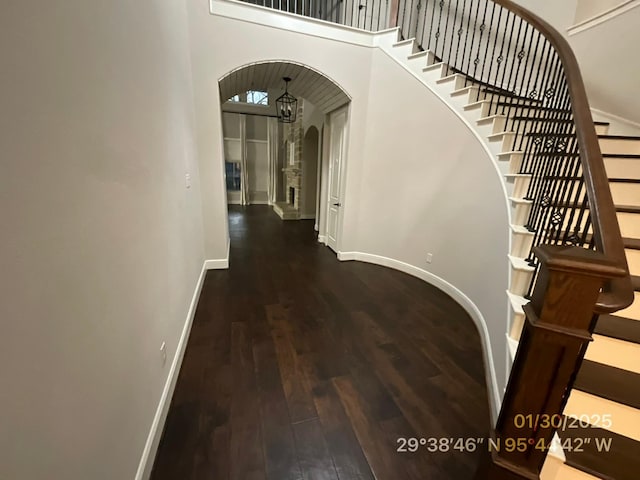 hall featuring arched walkways, a high ceiling, wood finished floors, baseboards, and stairway