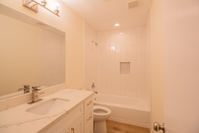 full bathroom with vanity, wood-type flooring, a textured ceiling, tiled shower / bath, and toilet