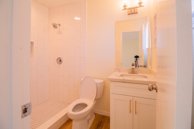 bathroom with hardwood / wood-style flooring, vanity, a tile shower, and toilet