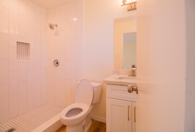 bathroom with vanity, tiled shower, hardwood / wood-style floors, and toilet