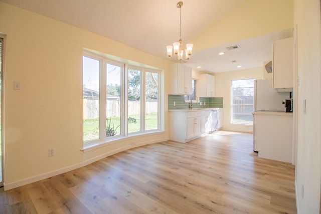 kitchen featuring a wealth of natural light, white cabinets, backsplash, and decorative light fixtures