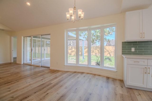 unfurnished dining area with vaulted ceiling, an inviting chandelier, and light hardwood / wood-style flooring