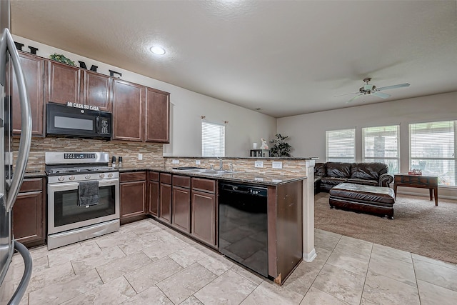 kitchen featuring sink, kitchen peninsula, dark stone counters, decorative backsplash, and black appliances