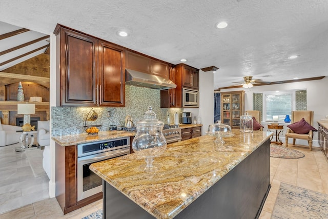 kitchen with range hood, appliances with stainless steel finishes, a kitchen island, light stone countertops, and decorative backsplash