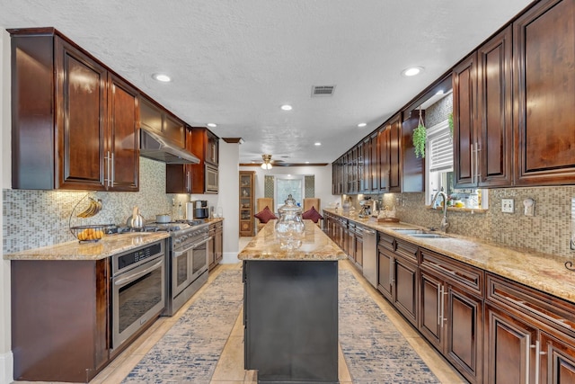 kitchen with sink, a center island, ceiling fan, stainless steel appliances, and light stone countertops