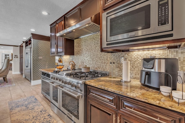 kitchen with high end appliances, wall chimney range hood, decorative backsplash, and light stone countertops