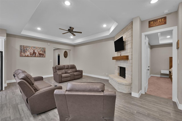 living room featuring hardwood / wood-style flooring, ceiling fan, a tray ceiling, and a stone fireplace