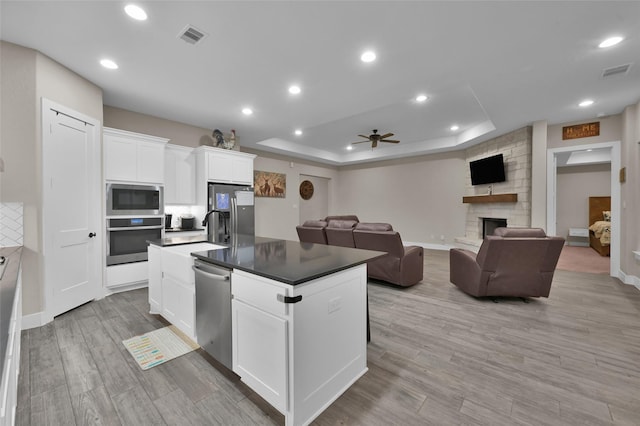 kitchen featuring white cabinetry, appliances with stainless steel finishes, a tray ceiling, a fireplace, and a kitchen island with sink