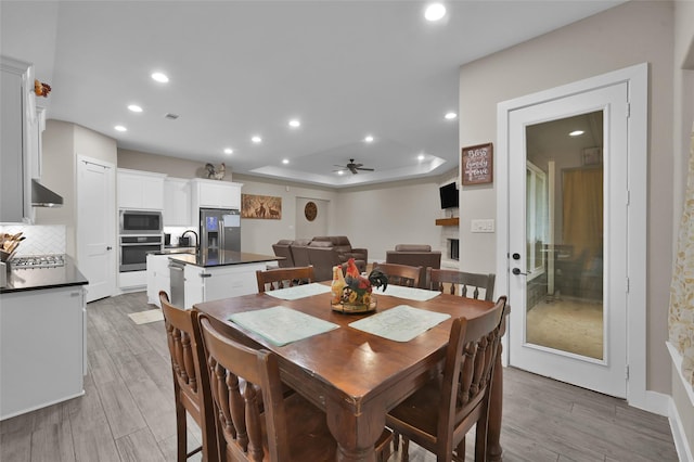 dining space featuring ceiling fan, a tray ceiling, and light hardwood / wood-style flooring