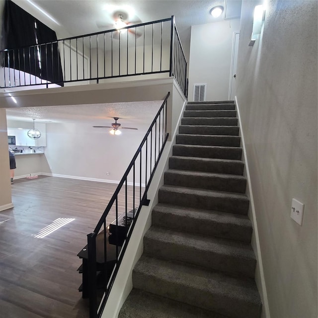 stairway with a towering ceiling, hardwood / wood-style floors, and ceiling fan