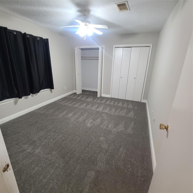 unfurnished bedroom with ceiling fan, two closets, a textured ceiling, and dark carpet