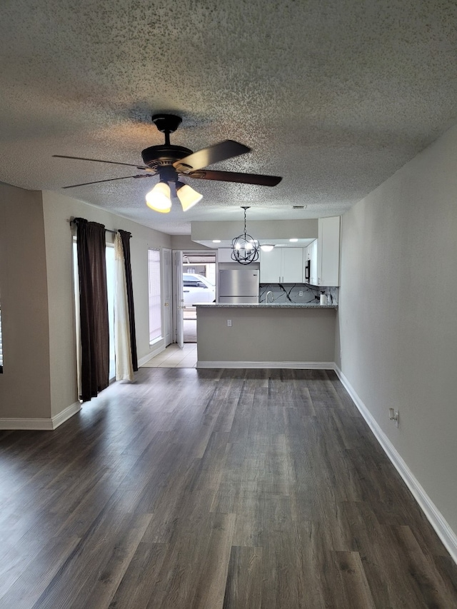 unfurnished living room with dark wood-type flooring, ceiling fan with notable chandelier, and a textured ceiling