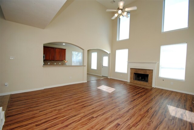 unfurnished living room with a fireplace, wood-type flooring, ceiling fan, and plenty of natural light