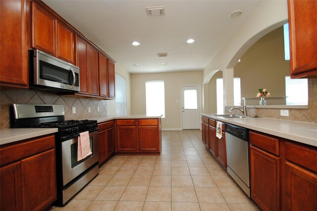 kitchen with tasteful backsplash, sink, light tile patterned floors, kitchen peninsula, and stainless steel appliances