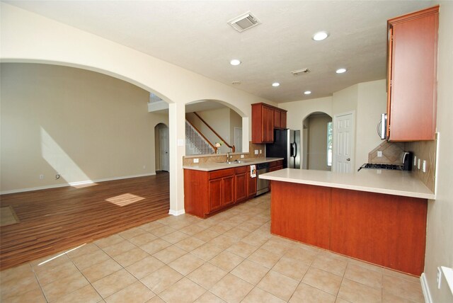 kitchen featuring appliances with stainless steel finishes, tasteful backsplash, sink, light tile patterned floors, and kitchen peninsula