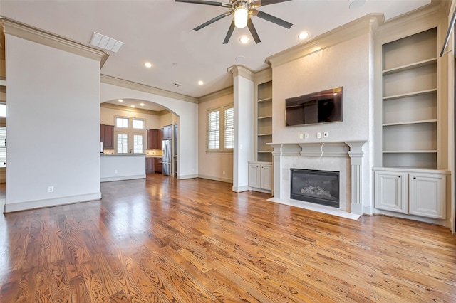 unfurnished living room featuring built in shelves, crown molding, ceiling fan, a high end fireplace, and light hardwood / wood-style floors