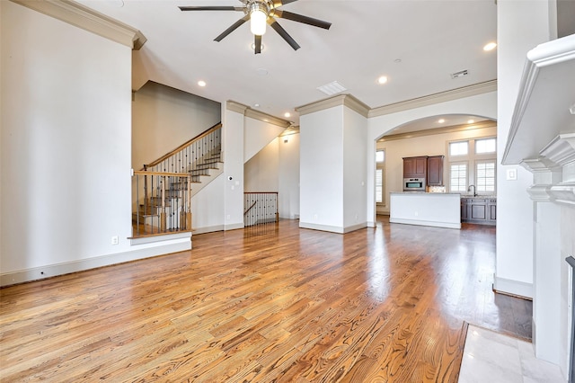 unfurnished living room with crown molding, sink, ceiling fan, and light wood-type flooring