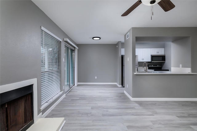 unfurnished living room featuring ceiling fan, sink, and light wood-type flooring