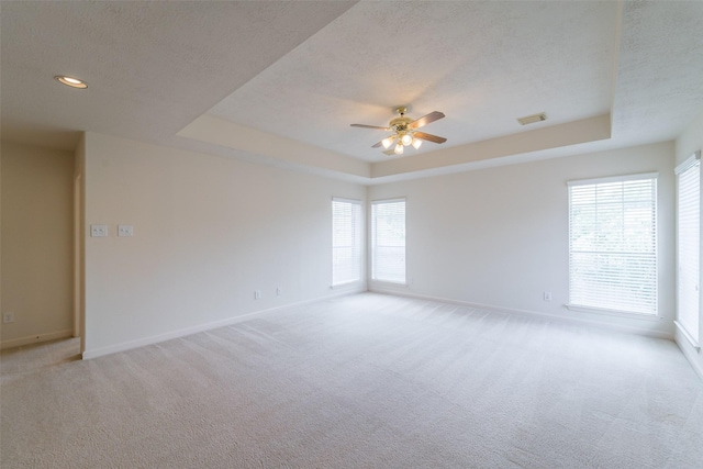 carpeted spare room featuring a raised ceiling, ceiling fan, and a textured ceiling