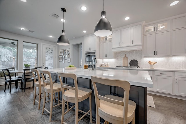 kitchen with a kitchen island with sink, light countertops, and glass insert cabinets