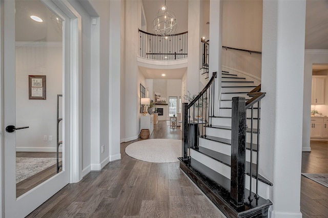 foyer featuring wood finished floors, baseboards, stairs, an inviting chandelier, and crown molding