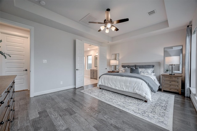 bedroom with connected bathroom, visible vents, baseboards, a raised ceiling, and dark wood finished floors