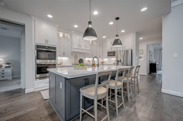 kitchen with stainless steel appliances, white cabinetry, light countertops, an island with sink, and decorative light fixtures