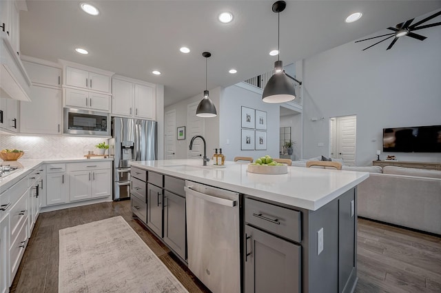 kitchen featuring open floor plan, stainless steel appliances, a kitchen island with sink, and white cabinets