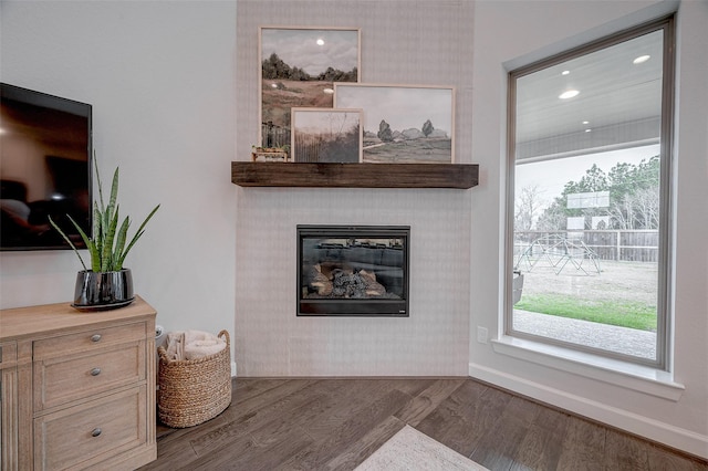 living area with a glass covered fireplace, plenty of natural light, wood finished floors, and baseboards