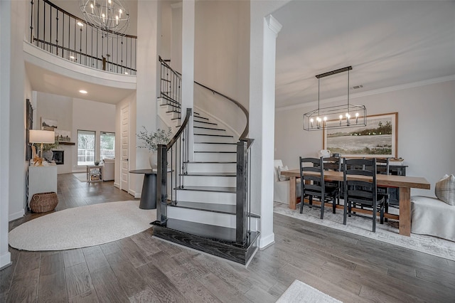 foyer featuring a towering ceiling, stairway, ornamental molding, wood finished floors, and a notable chandelier