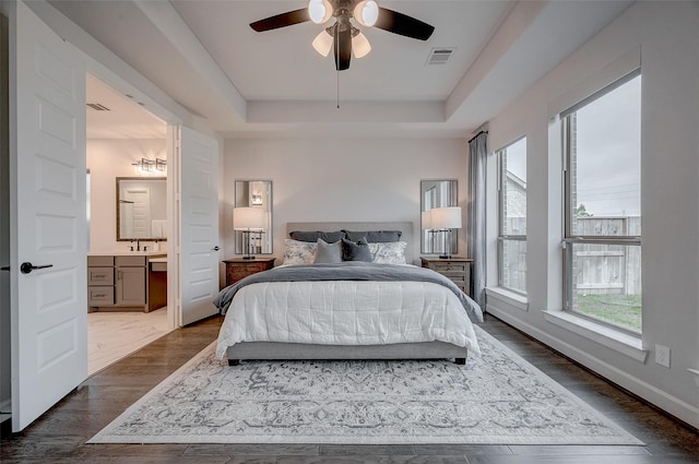 bedroom with a raised ceiling, visible vents, baseboards, and ensuite bathroom