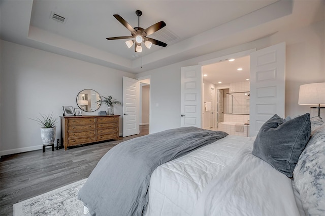 bedroom with visible vents, baseboards, ensuite bath, wood finished floors, and a tray ceiling