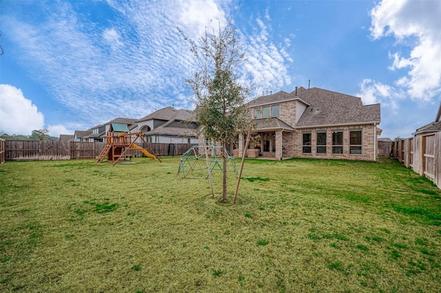 rear view of property with a fenced backyard, a lawn, a playground, and brick siding