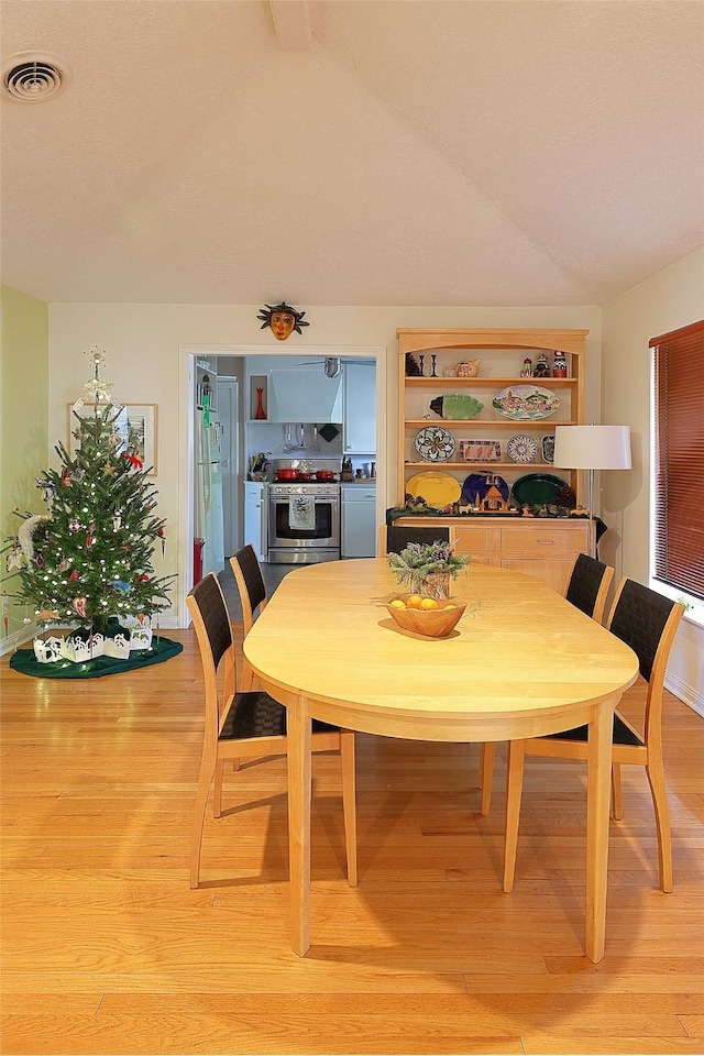 dining room featuring visible vents, vaulted ceiling, and light wood finished floors