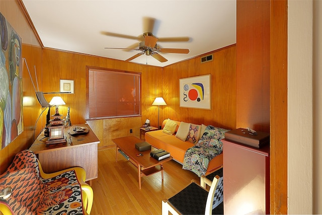 living area with wooden walls, wood finished floors, visible vents, and a ceiling fan