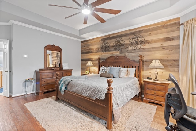 bedroom featuring ceiling fan, wood walls, wood finished floors, and a raised ceiling