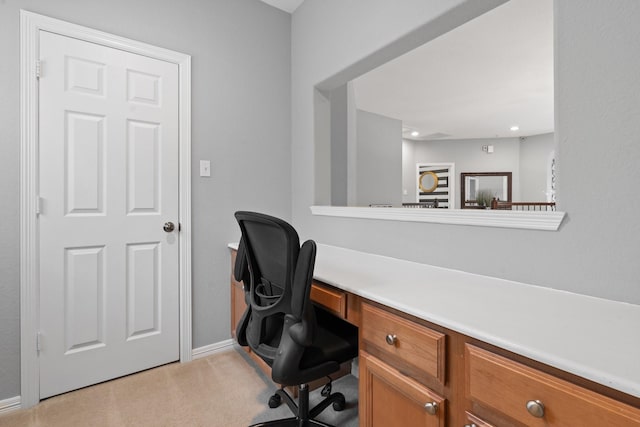 home office with baseboards, built in desk, and light colored carpet