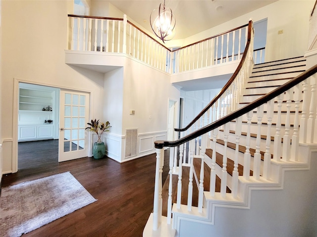 staircase with a decorative wall, a wainscoted wall, wood finished floors, visible vents, and an inviting chandelier