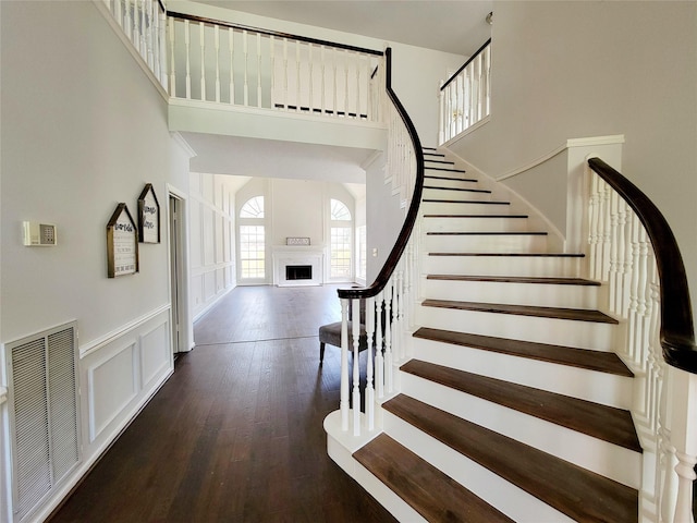 stairway featuring visible vents, a decorative wall, a high ceiling, and wood finished floors