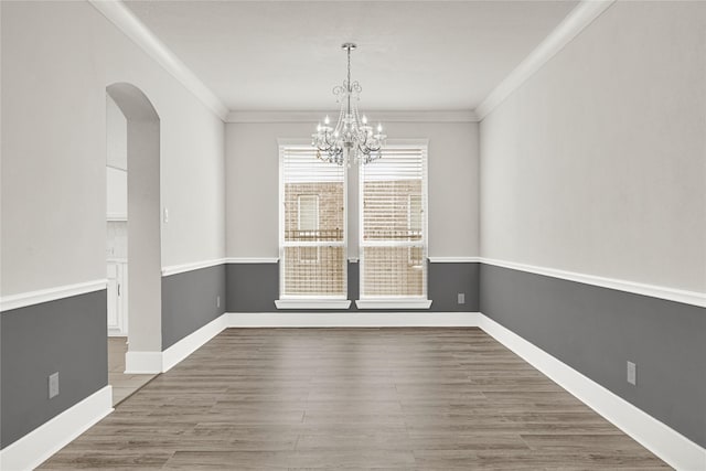 unfurnished dining area featuring a chandelier, ornamental molding, arched walkways, and wood finished floors