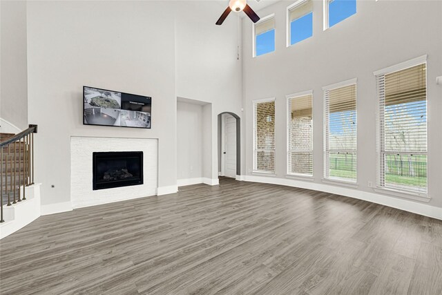 unfurnished living room with stairway, wood finished floors, a ceiling fan, baseboards, and a fireplace