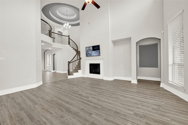 unfurnished living room with baseboards, stairway, ceiling fan with notable chandelier, wood finished floors, and a raised ceiling