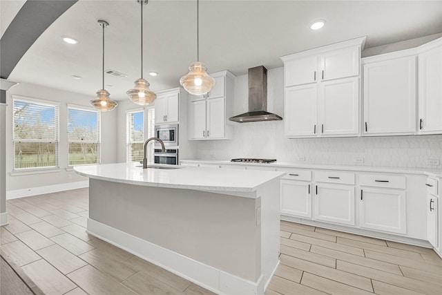 kitchen with stainless steel microwave, wall chimney range hood, backsplash, and gas cooktop