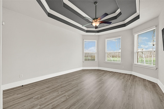 unfurnished room with a ceiling fan, a tray ceiling, wood finished floors, and baseboards