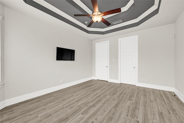 unfurnished bedroom featuring a raised ceiling, wood finished floors, visible vents, and baseboards