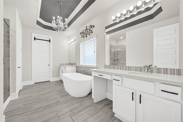 full bath featuring an inviting chandelier, a tray ceiling, two vanities, a stall shower, and a sink