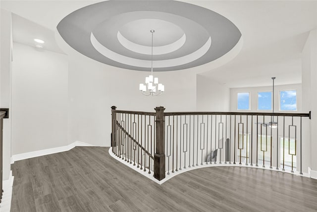 stairway with an inviting chandelier, wood finished floors, baseboards, and a raised ceiling