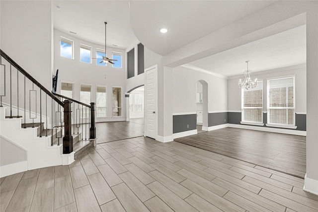 entrance foyer with arched walkways, stairway, ceiling fan with notable chandelier, and wood finish floors