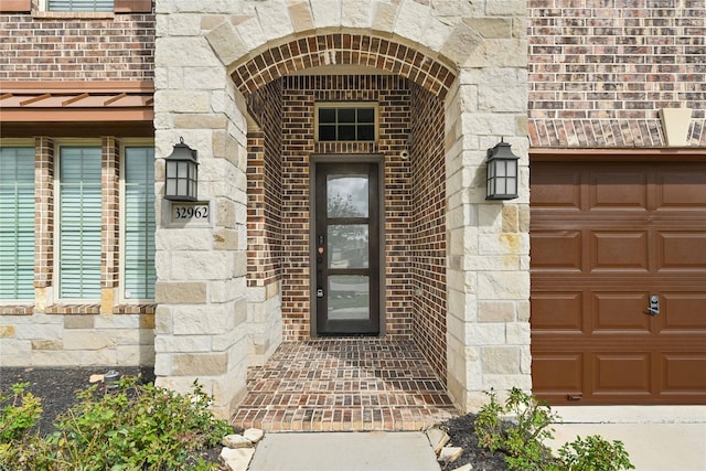 entrance to property featuring brick siding, a garage, and stone siding