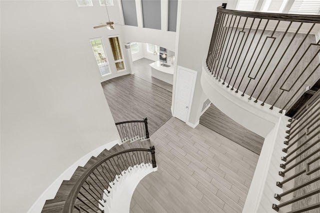 stairway featuring a ceiling fan, wood finished floors, baseboards, and a towering ceiling